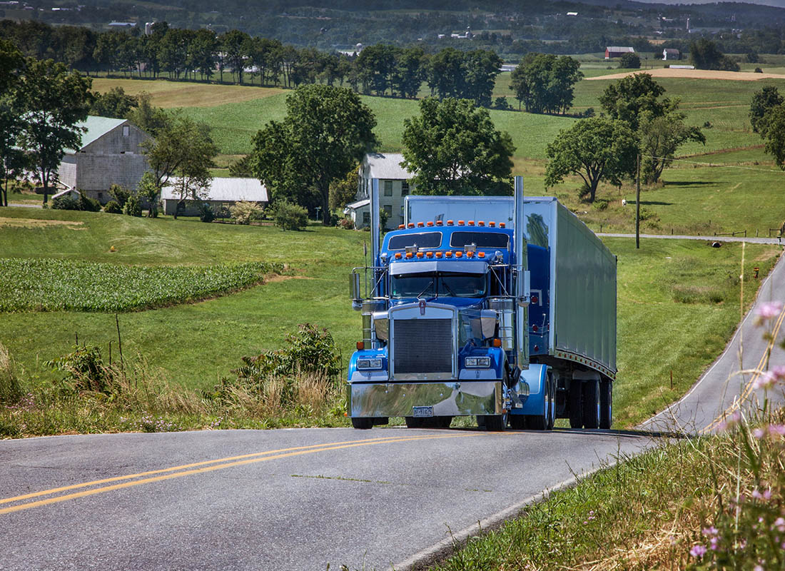 Insurance Solutions - Blue Tractor Trailer Truck Driving Up a Country Road on a Sunny Day
