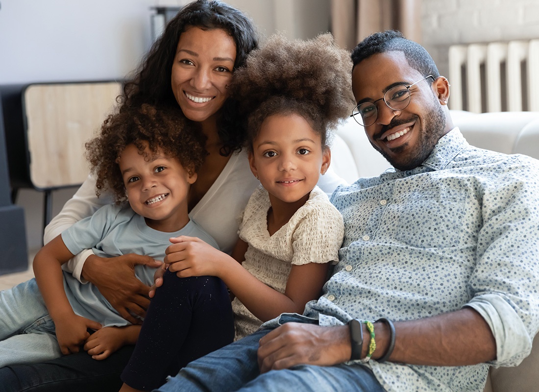 Personal Insurance - Happy Family and Their Two Young Children Sit Together and Smile at Home